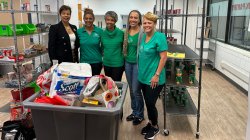 Five women volunteers standing in pantry with bin filled with donated supplies.