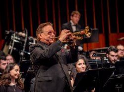 Arturo Sandoval plays the trumpet with 青青草app in the University Wind Symphony seated behind him.