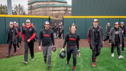 Men in black-and-red app baseball uniforms walk onto a field.